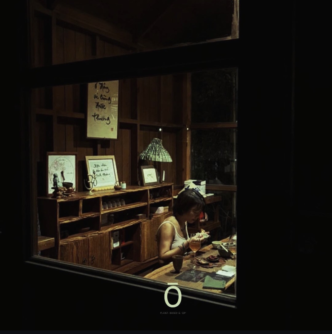 Ōmao — warm timber dining room seen through the window at night, a guest at the counter under lamp light